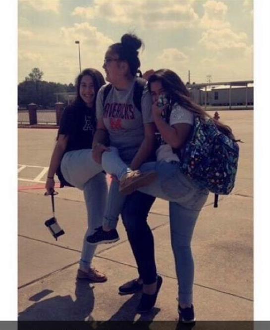 Three friends strike a fun pose, lifting their legs and enjoying a sunny day outside.
