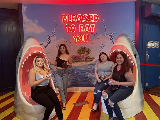 A group of four friends poses together at a colorful shark-themed installation.