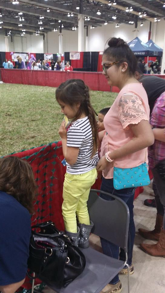 Two children and adults watch activities at a busy community gathering event indoors.