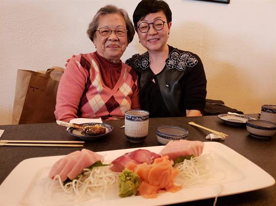 Two women share a joyful moment at a table with a colorful sushi platter in front of them.
