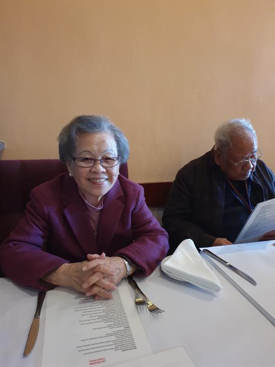 An elderly couple sits at a table, reviewing the menu in a warm restaurant setting.