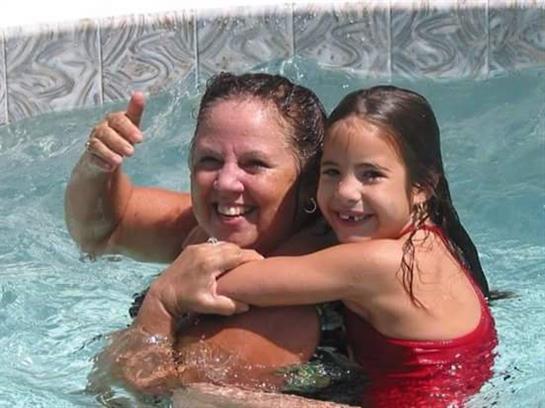 Grandmother and granddaughter are having fun in the pool while smiling and splashing water.