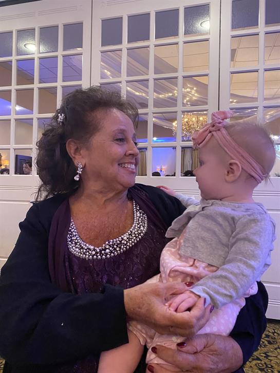 A joyful elderly woman smiles while holding a baby girl in a beautiful venue filled with family.