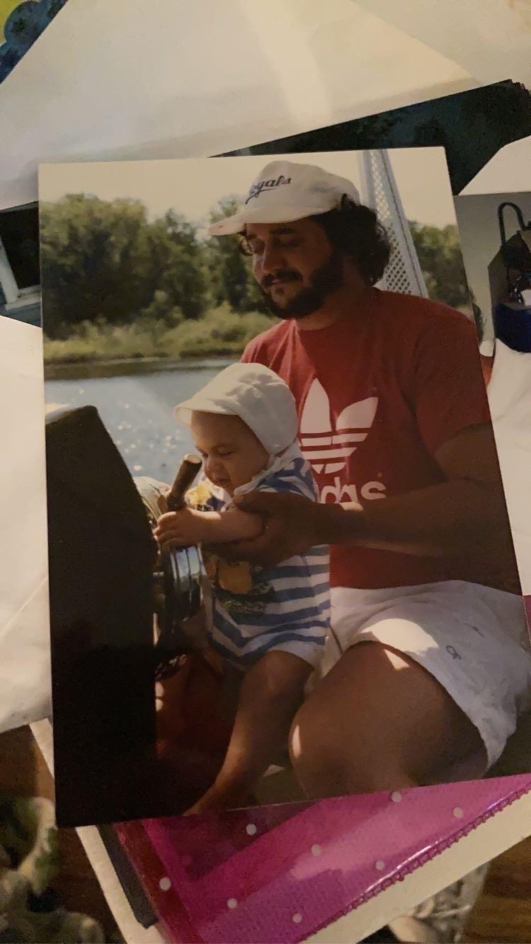 A father and his baby share a joyful moment steering a boat on a sunny day by the water.