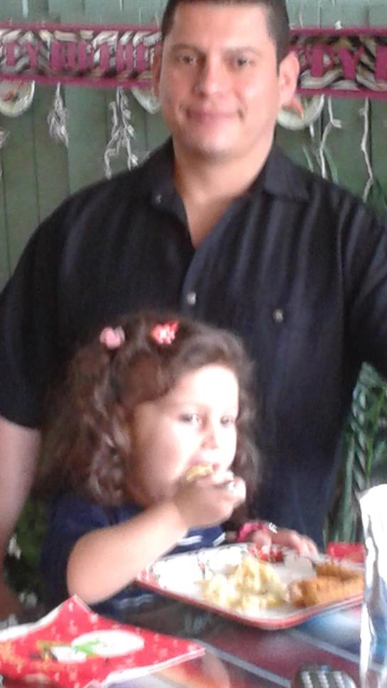 A young girl happily eats while standing beside an adult in a festive atmosphere.