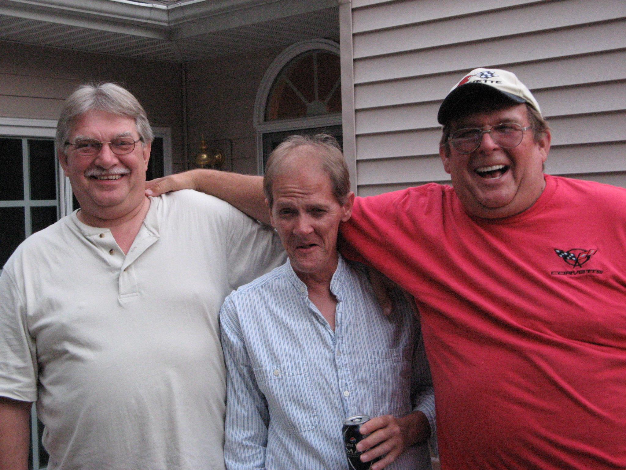 Three men share a joyful moment outdoors in a sunny backyard, creating memories together.