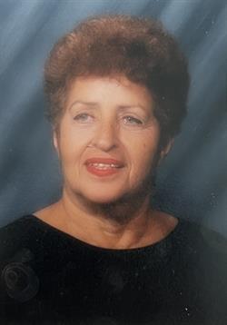 A woman with curly hair and a friendly smile is photographed against a soft blue background.