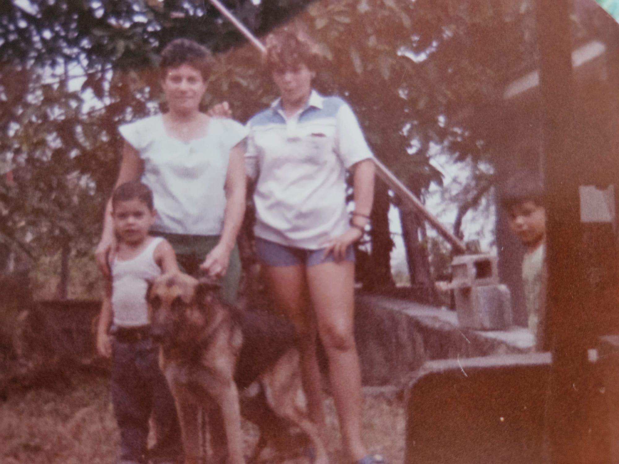 Two women stand beside a boy and a dog in a lush green environment, enjoying family time.