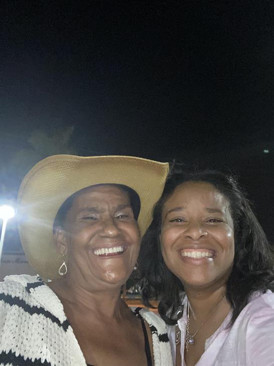 Two women smile broadly while posing together at a vibrant outdoor event during the evening.