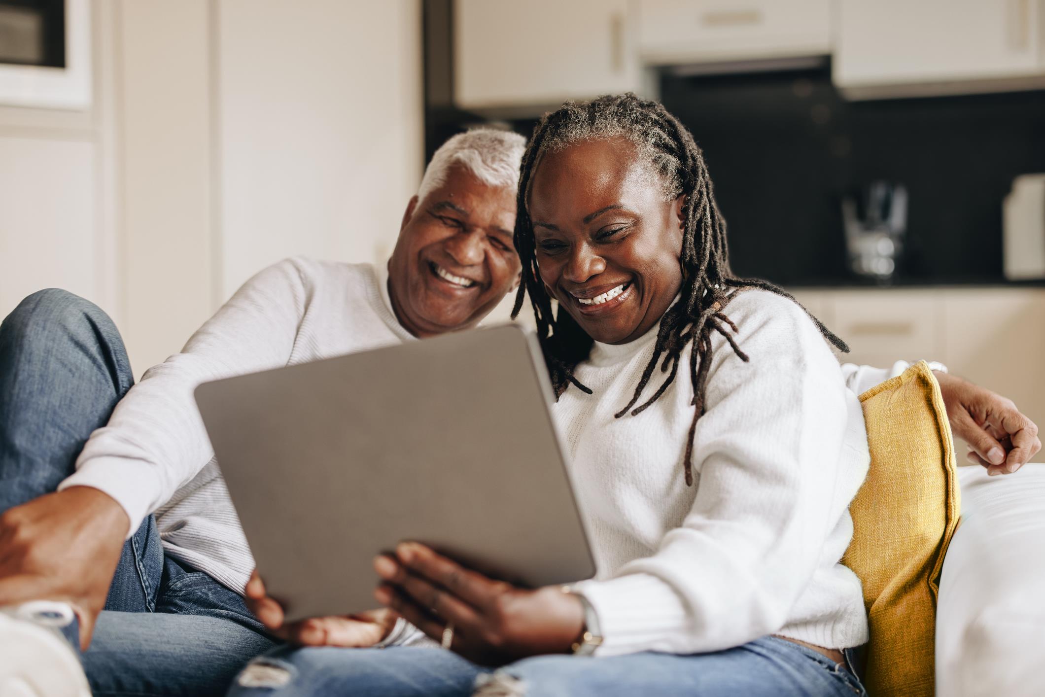 Two seniors share a joyful moment, looking at a laptop screen, smiling and relaxed indoors.