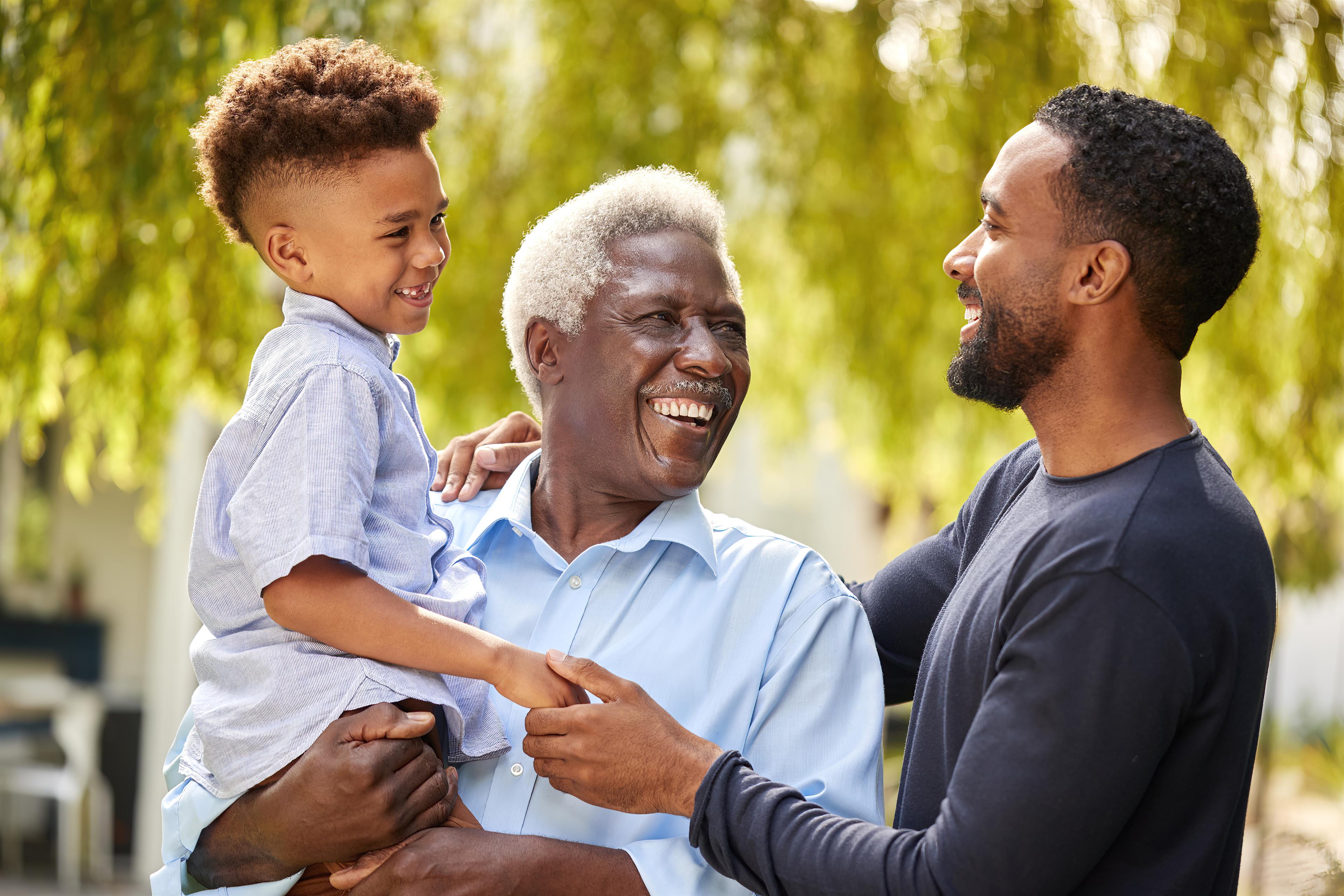 Three generations share laughter and joy together in a warm, sunny park setting.