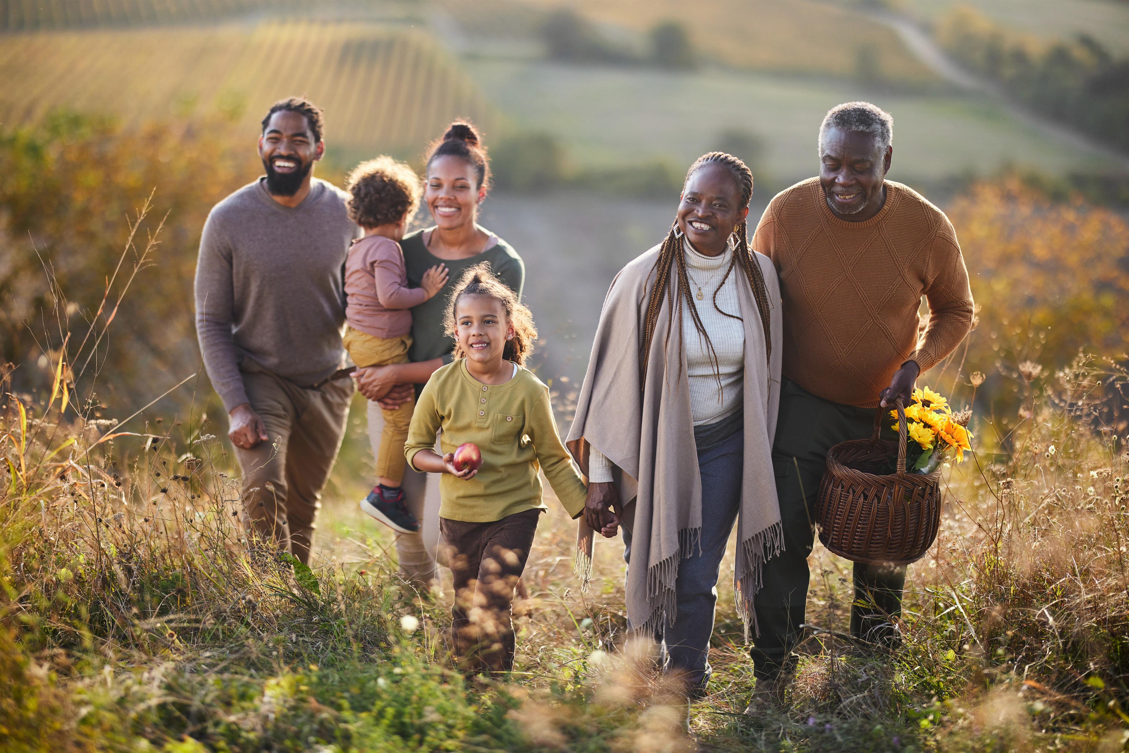 Five family members smile and chat as they stroll through tall grass in a lovely landscape.