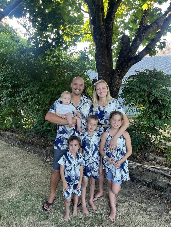 A family enjoys time together outside, wearing coordinating floral shirts and dresses amid greenery.