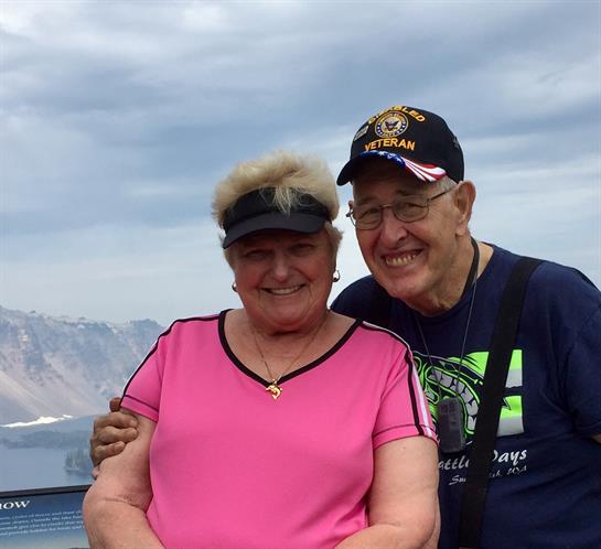 Two seniors joyfully pose together at a beautiful outdoor location with mountains behind.