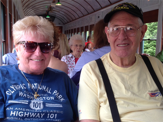 A cheerful couple sits close together on a train, enjoying their journey and each other's company.