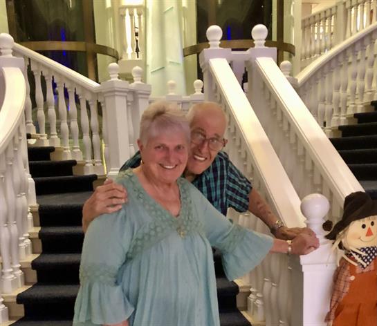 A joyful elderly couple smiles as they pose near a charming staircase with decorations.