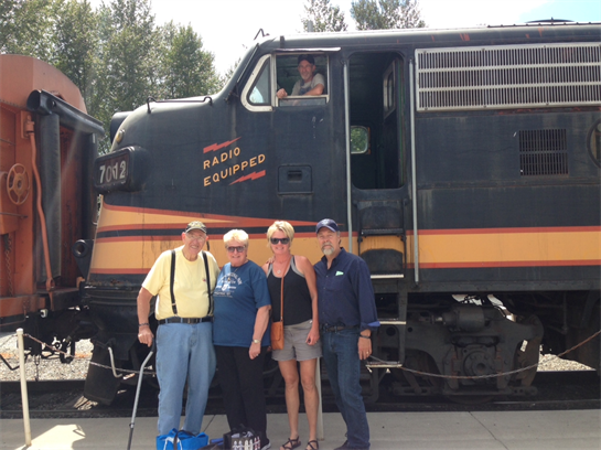 Friends gather next to an antique train, enjoying their time at the station on a sunny day.