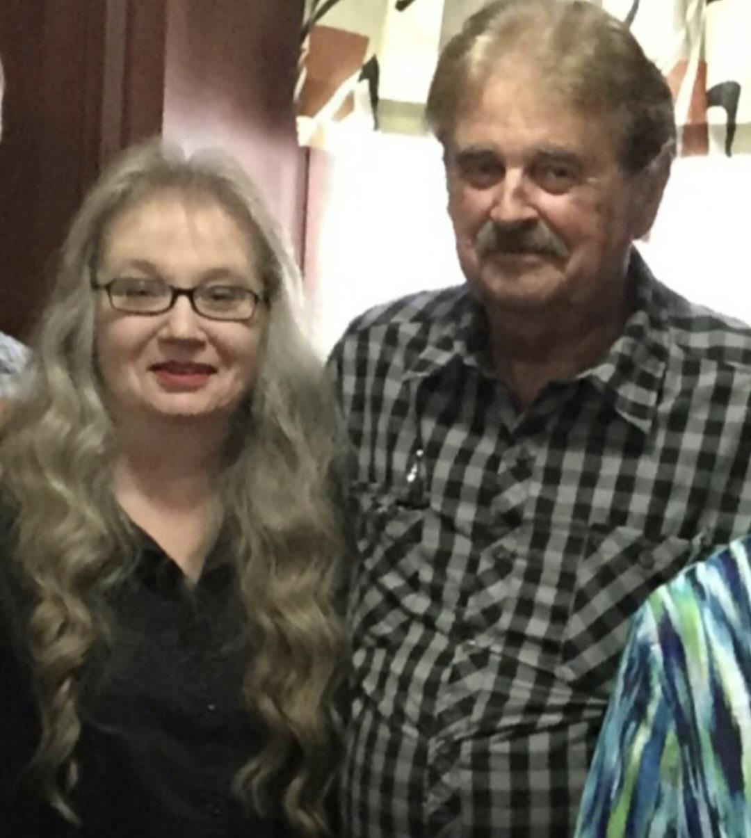 Two individuals with joyful expressions stand side by side in a warmly lit room.