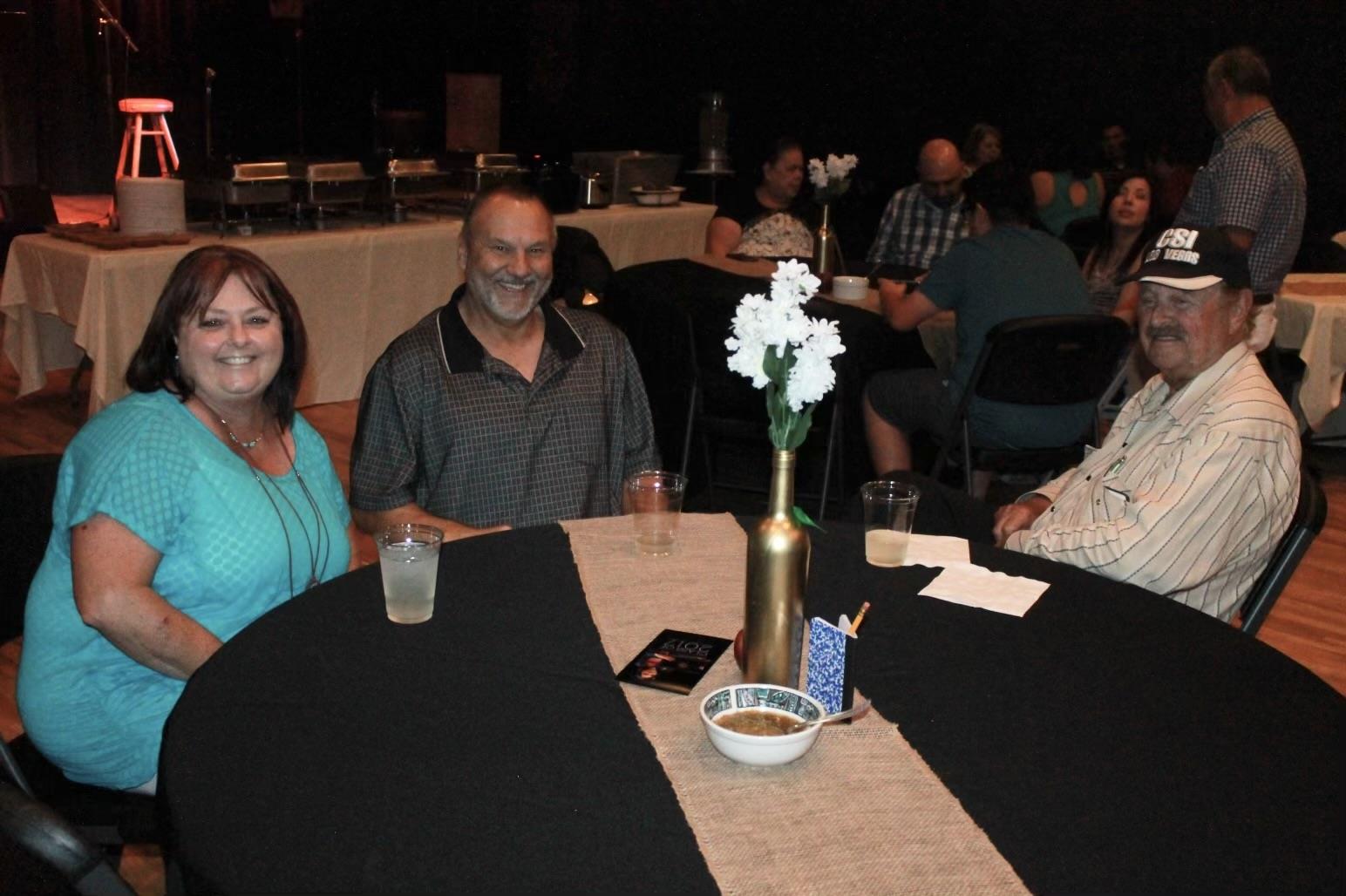 Three friends gather around a table, engaging in cheerful conversation at a lively event.