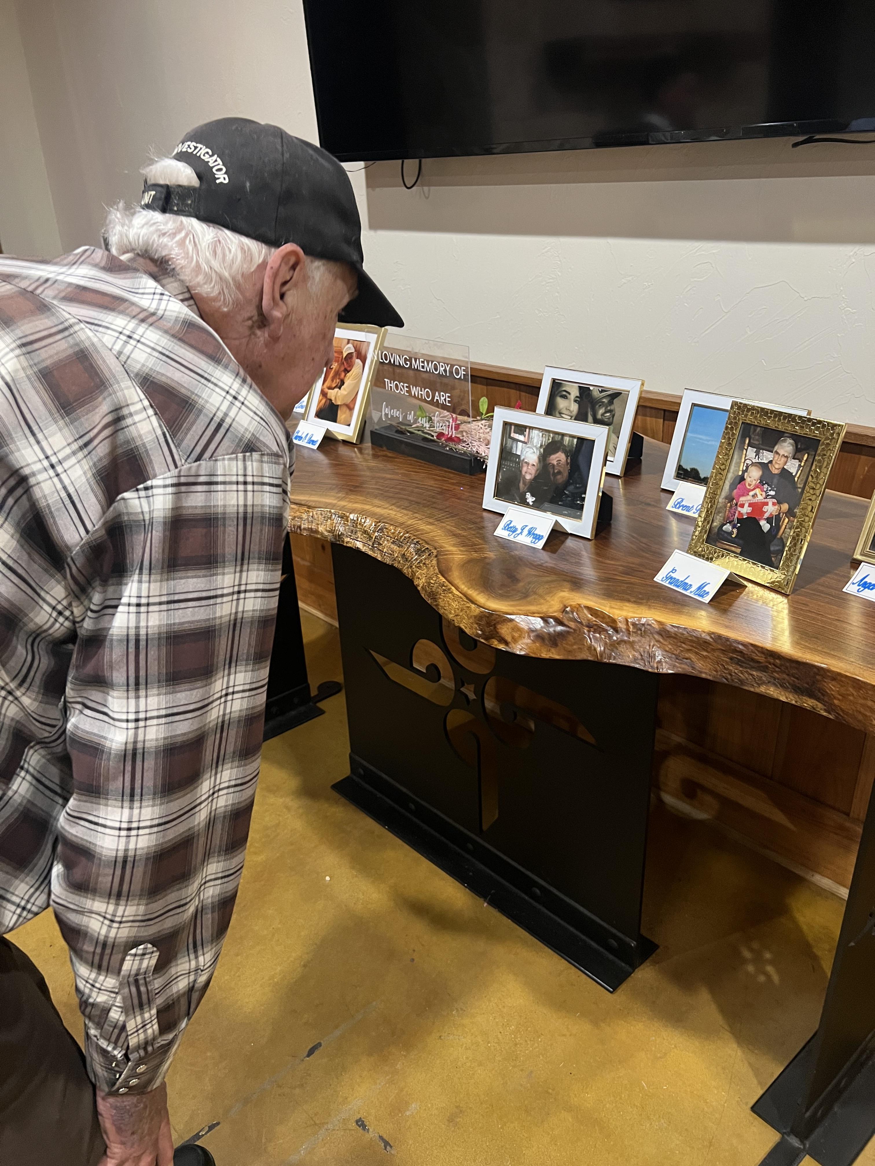 A senior man leans forward to closely inspect family portraits on a beautifully crafted table.