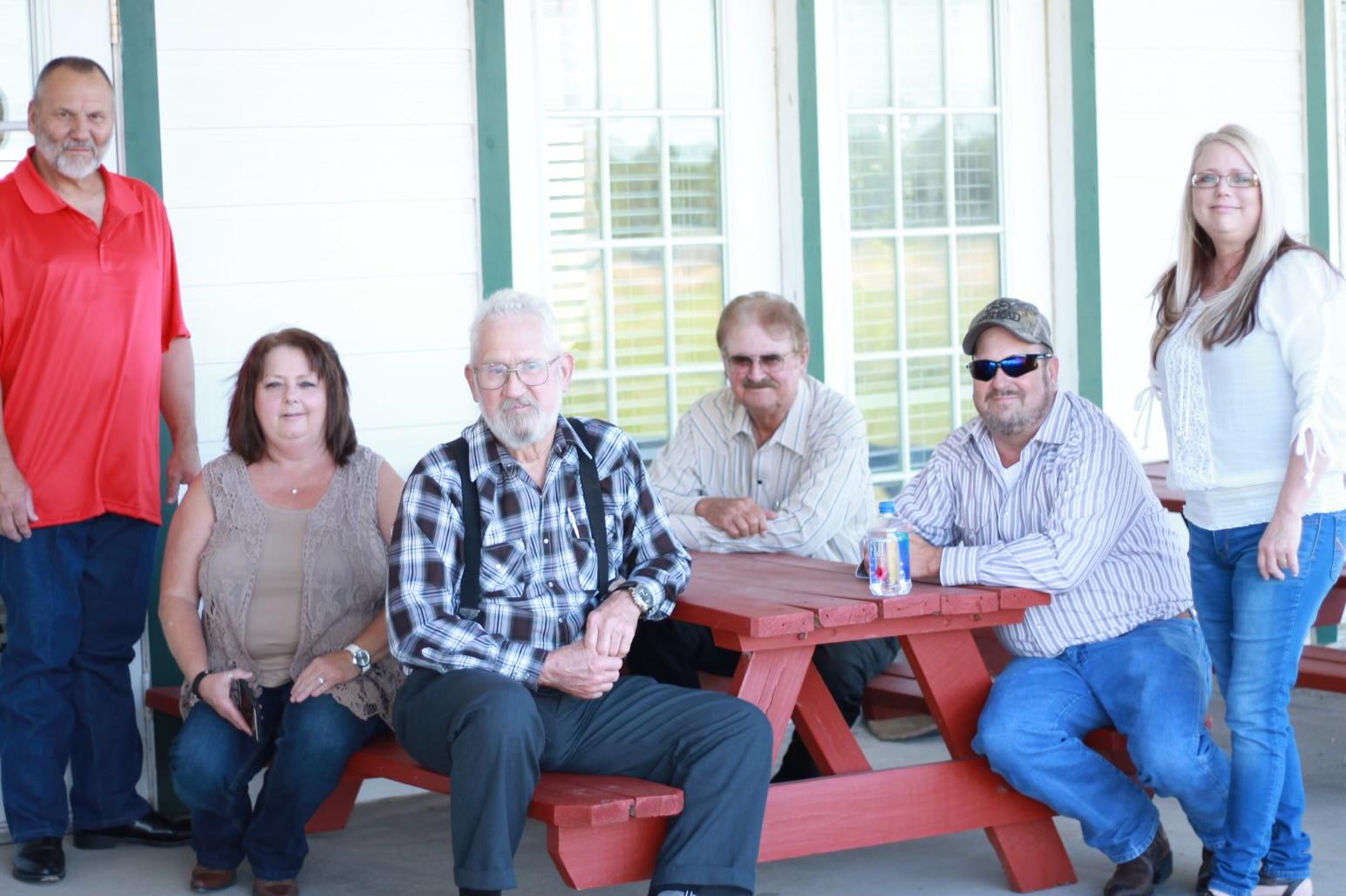 Six people gather at a red picnic table, sharing good times and laughter on a sunny day.