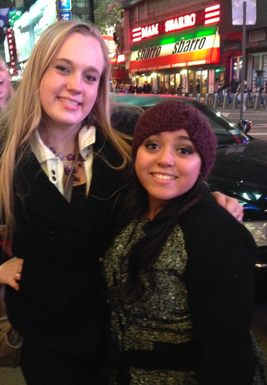 Friends smile and enjoy a cheerful moment in Times Square, surrounded by vibrant lights.