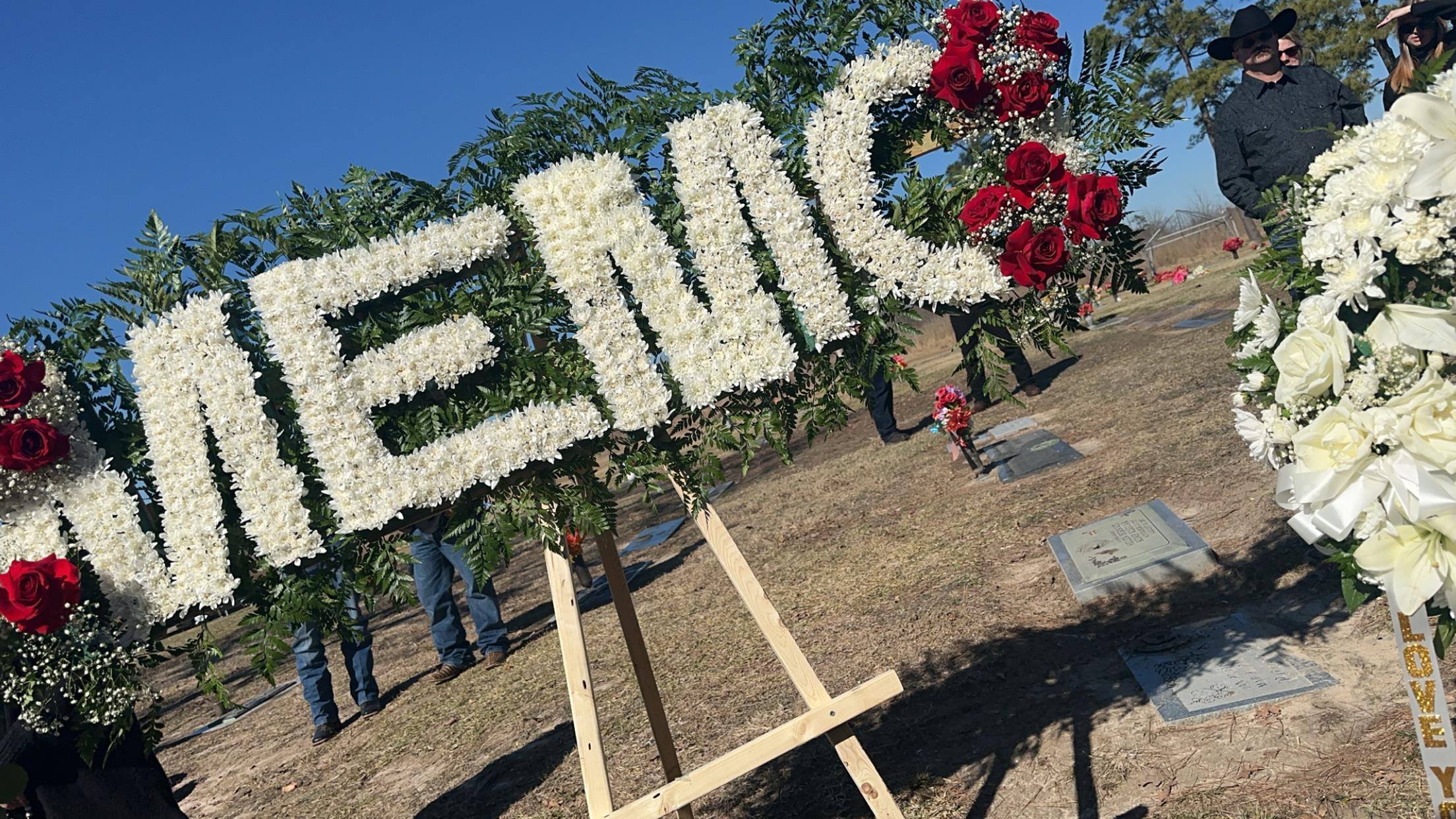 A vibrant display of flowers forms the letters MEMC at a memorial service in a serene cemetery.