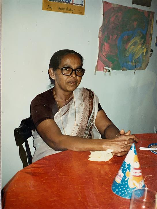 An elderly woman in traditional attire smiles at a festive table, enjoying the event.