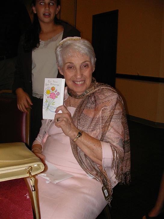 Elderly woman proudly displays a colorful handmade card while seated, smiling warmly.