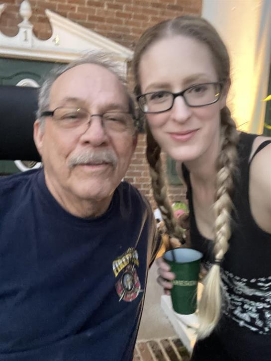 A senior man and a young woman smile together while relaxing outdoors during sunset.