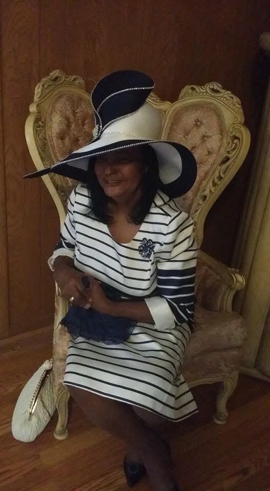 Woman wears a chic striped dress and oversized hat while sitting gracefully in an elegant chair.