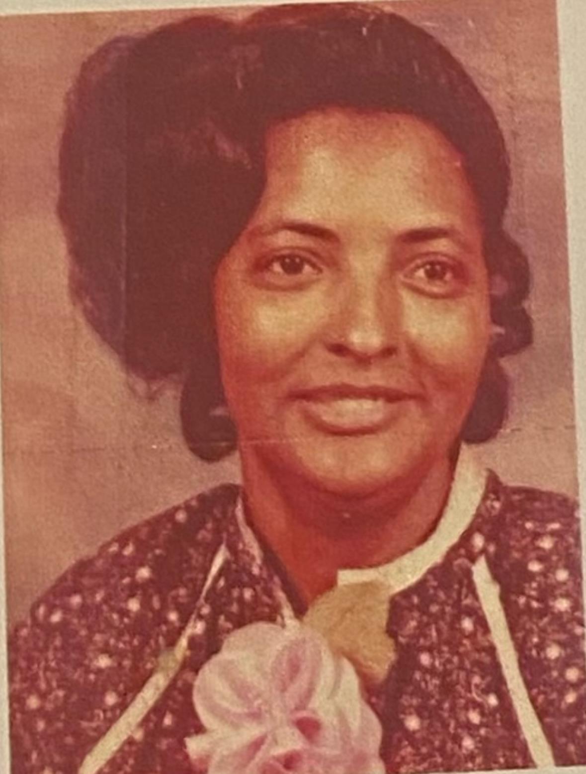 Woman poses calmly in a vintage outfit with a floral accessory, radiating grace and elegance.