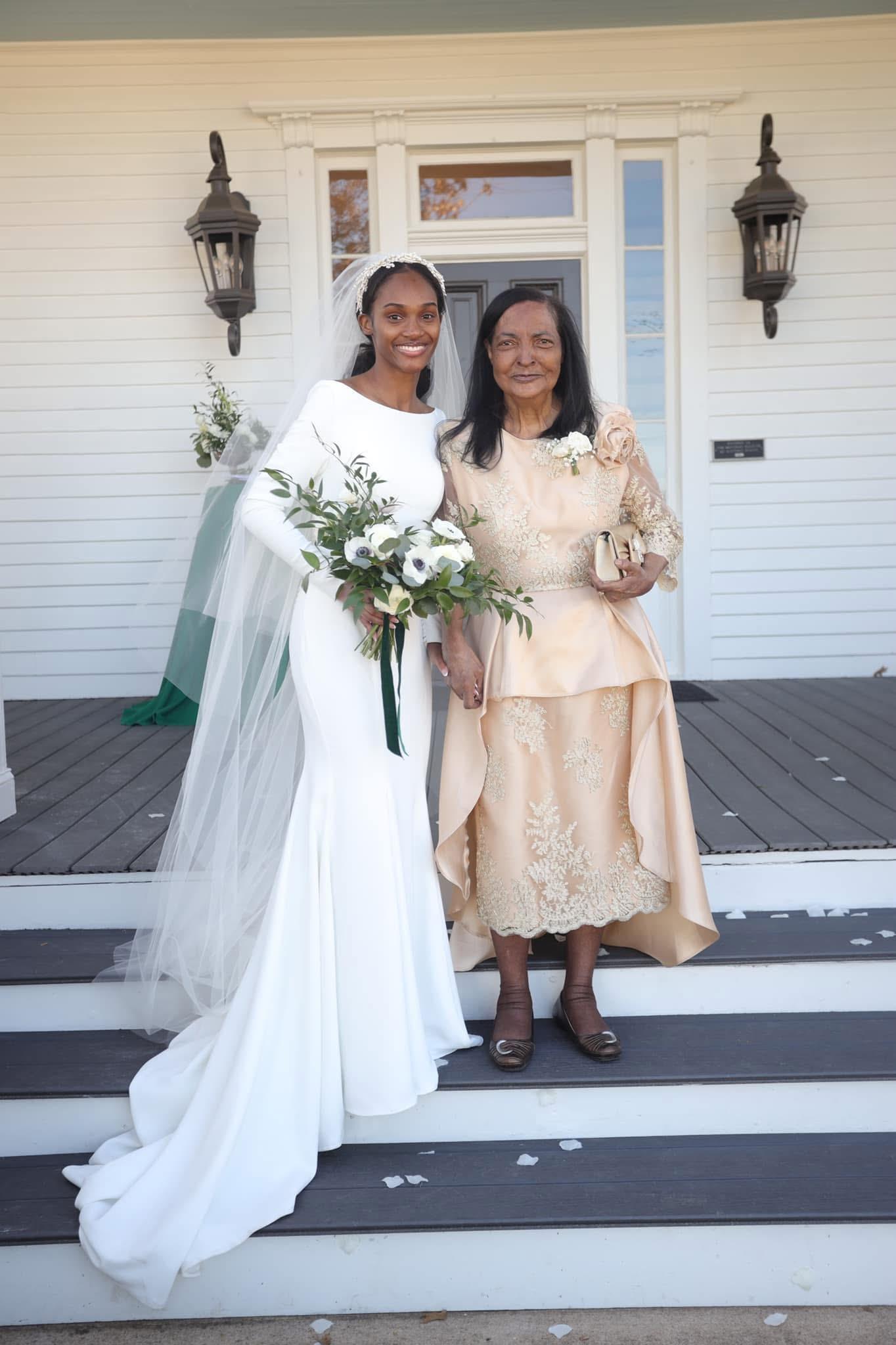 A joyful bride poses with her mother, both beaming in stylish outfits, on wooden steps.