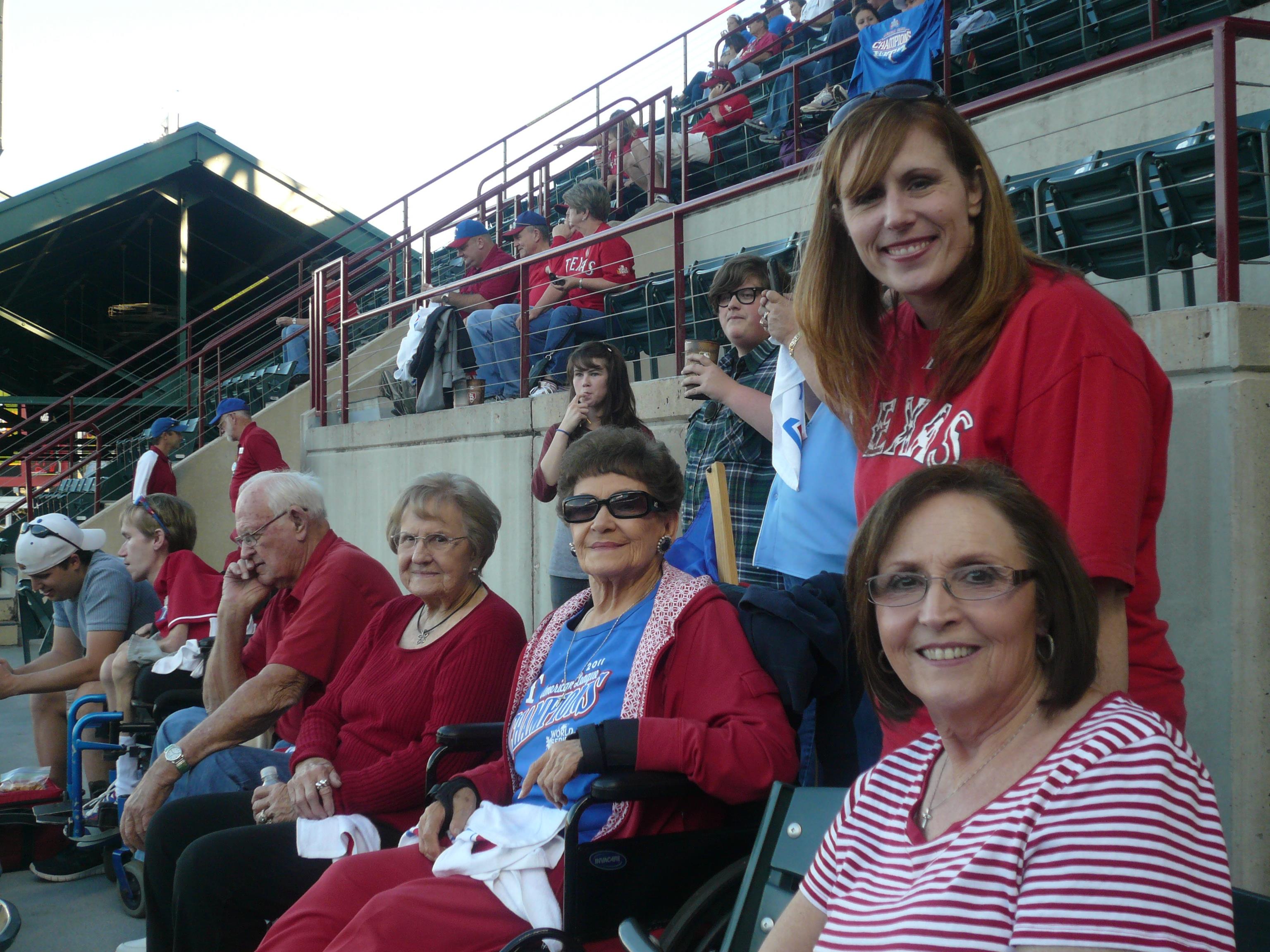 Seniors gather in stadium seats, smiling and wearing team colors while watching a game.