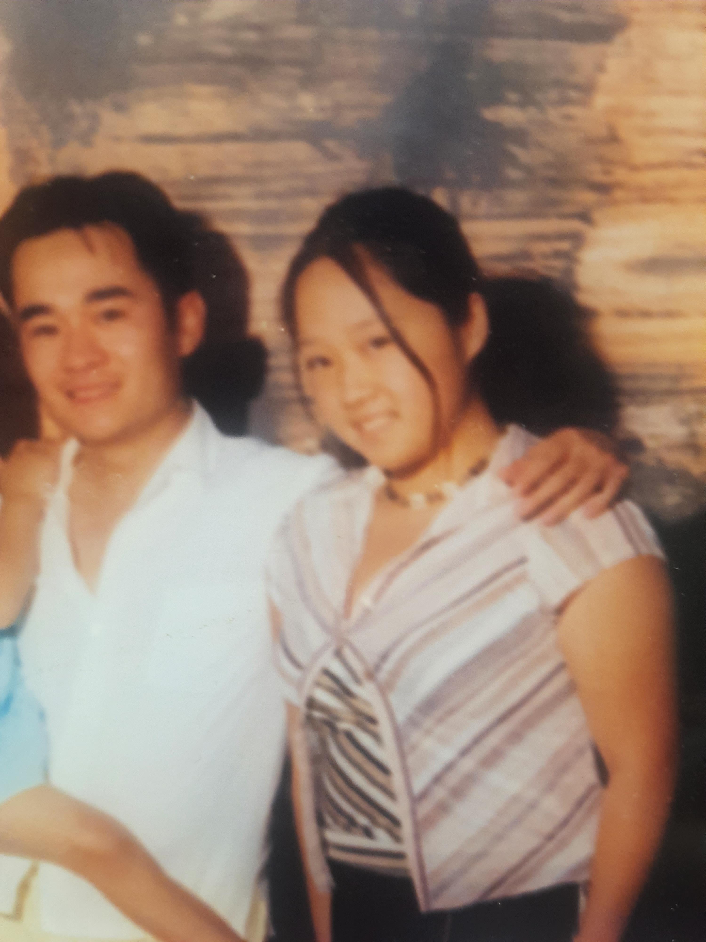 Two friends happily pose together at a beach with warm sunlight glowing in the background.