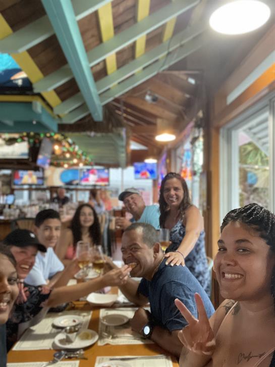 Friends gather around a table, sharing laughter and food in a vibrant seaside eatery.