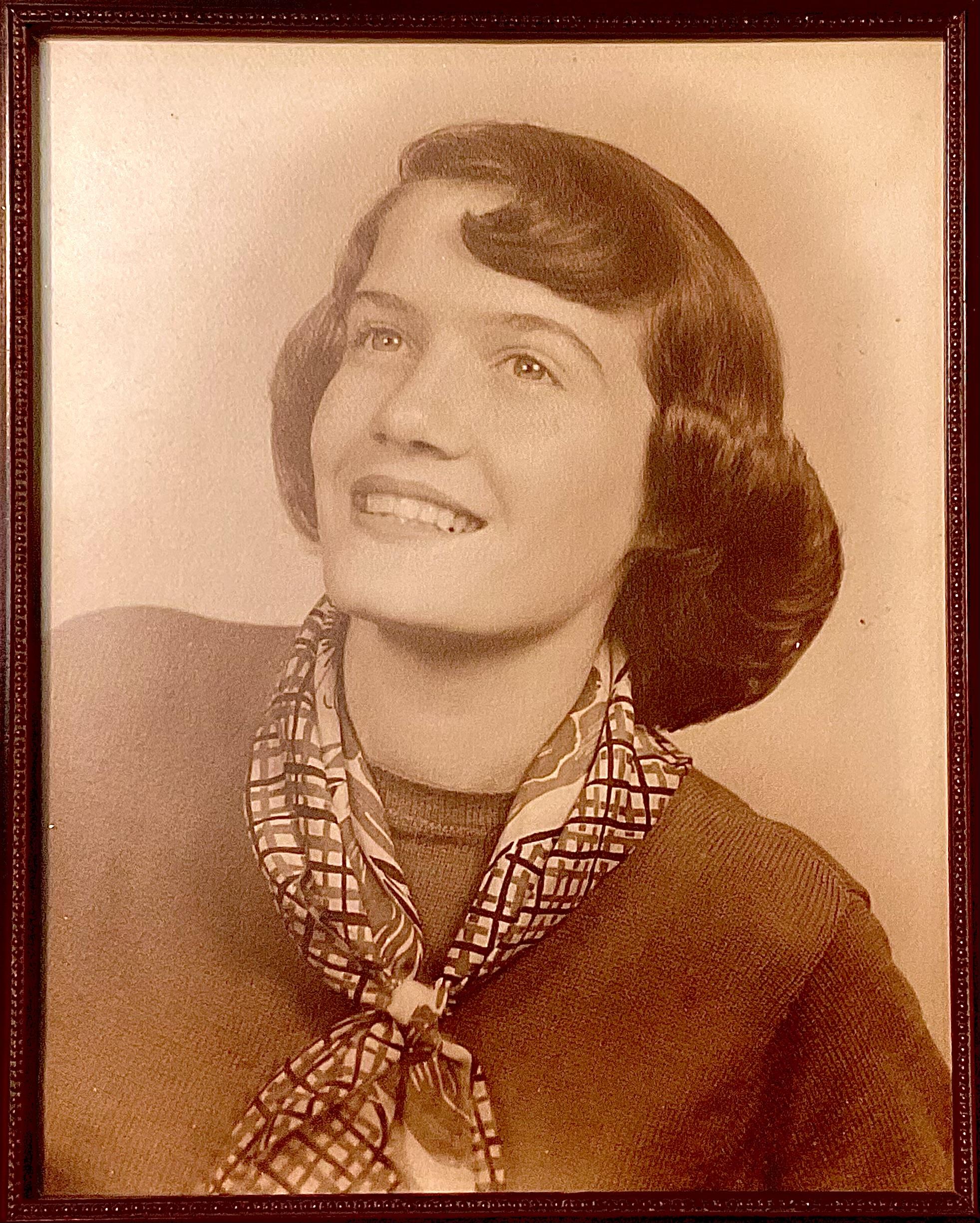 A charming portrait of a woman with a vintage hairstyle and stylish scarf, radiating warmth.