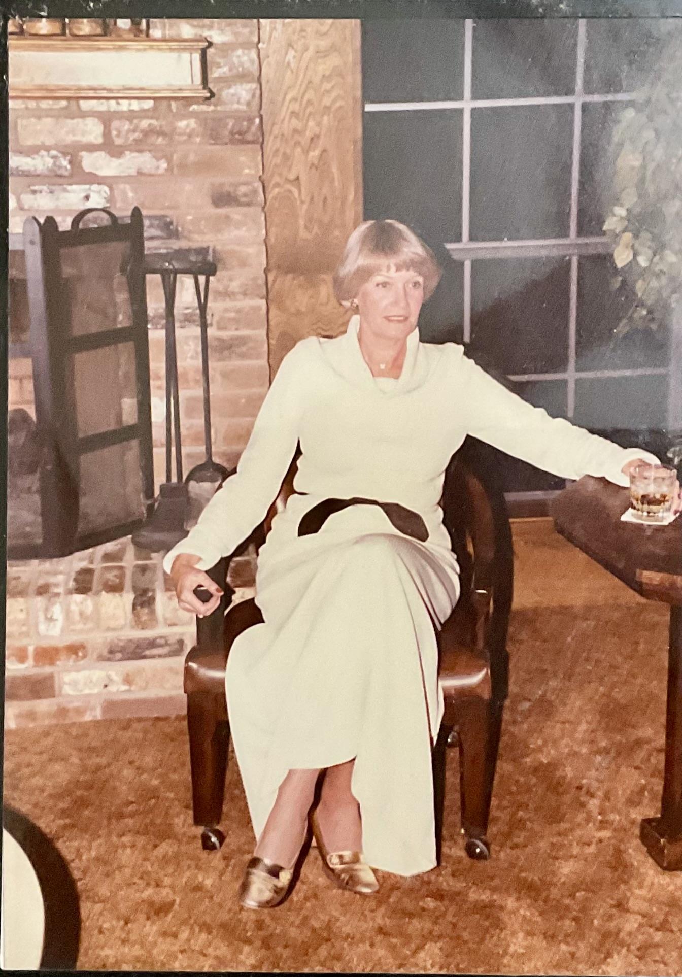 A woman dressed in white sits comfortably in a vintage living room with a cozy atmosphere.
