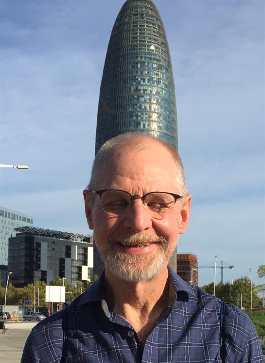 Elderly man with glasses enjoys a sunny day in front of contemporary building in city.