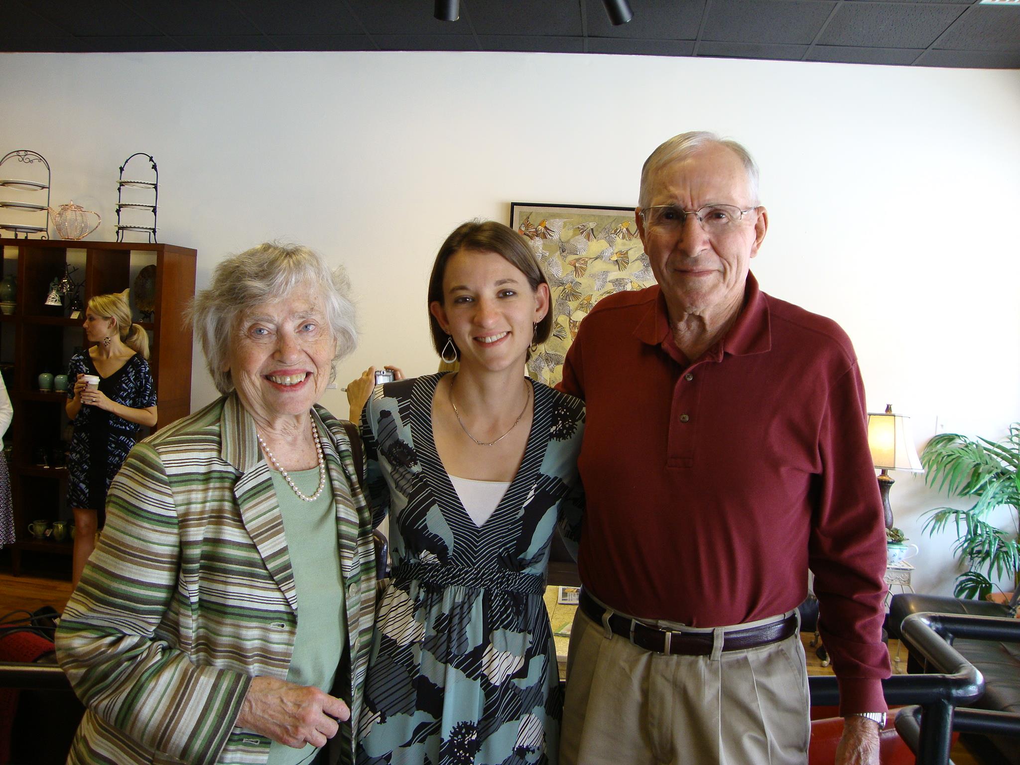 A joyful gathering takes place as a woman stands between an elderly couple, all smiling warmly.
