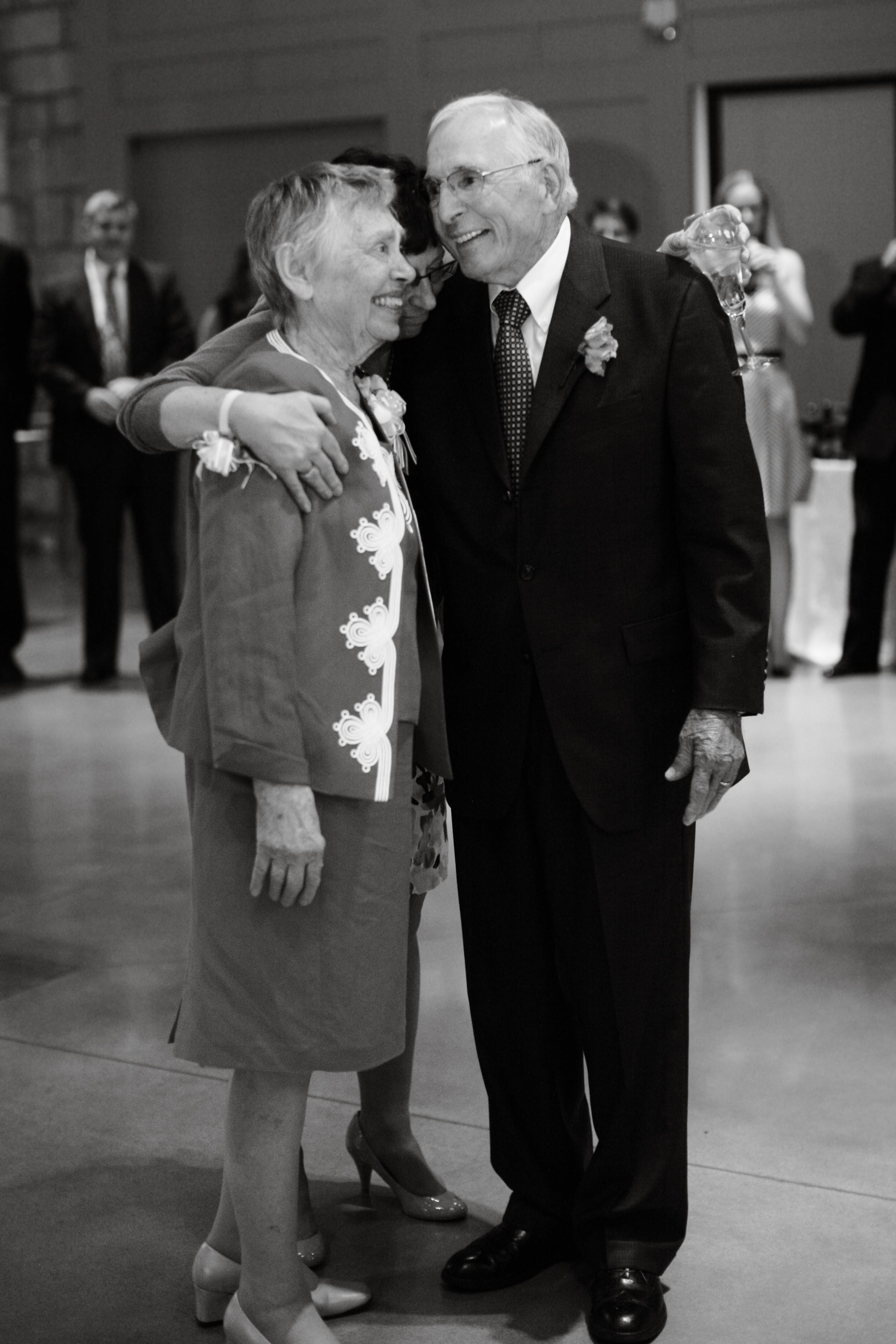 Couple dressed in formal attire smiles at each other during a festive event in a banquet hall.