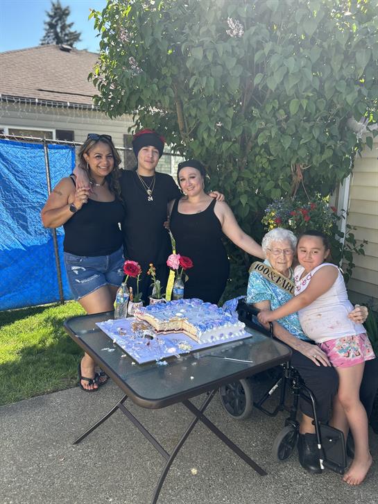 Four family members gathered around a decorated table celebrating with a cake and flowers.
