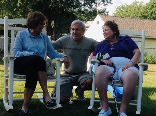 Three friends relax and share laughter on a warm sunny day in a backyard.