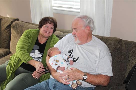 Grandparents enjoy a heartwarming moment with their newborn grandchild on a couch.