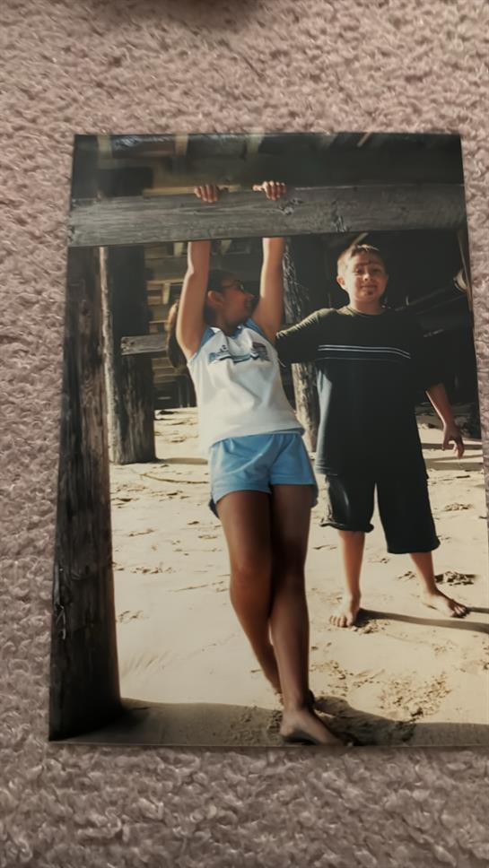 Two children enjoy a playful moment at the beach, hanging from a wooden post by the shore.