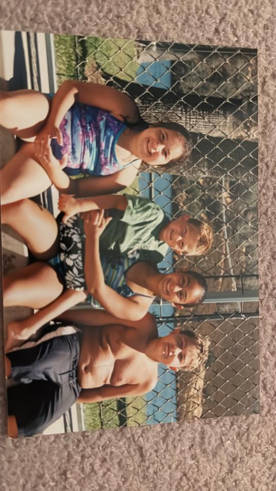 Four children are smiling and posing together, enjoying time after swimming.