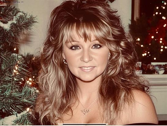 A woman with curly hair smiles in a cozy, decorated room during the holiday season.