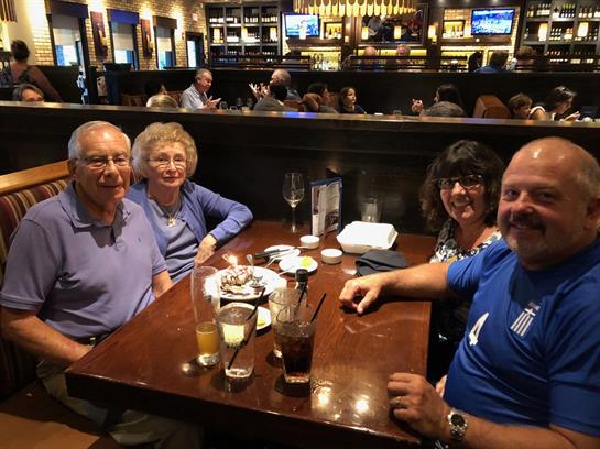 Four friends share laughter and conversation over drinks and dessert at a restaurant.
