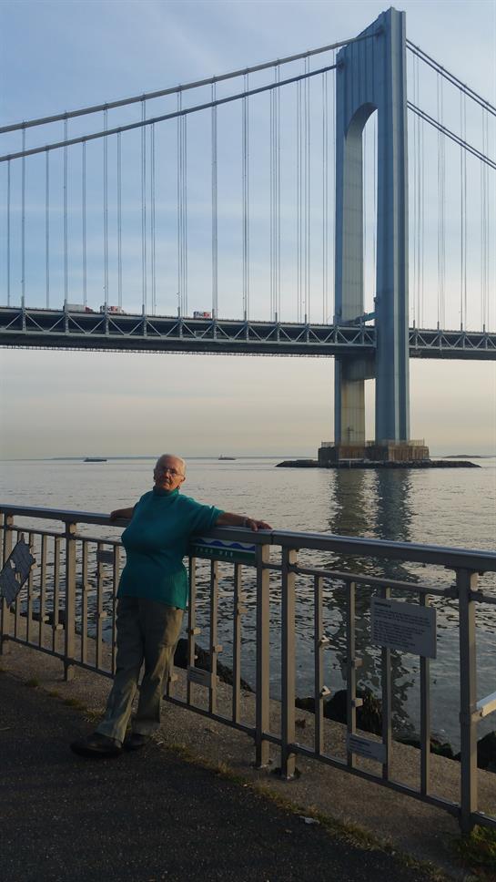 Individual enjoys quiet morning by the water, gazing at a large suspension bridge in the distance.