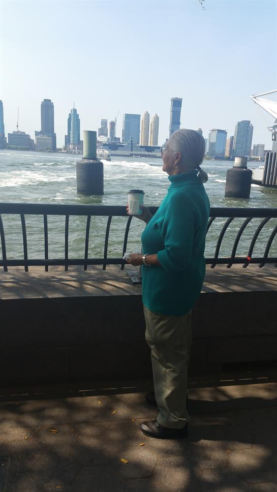 A woman stands by the water, sipping coffee and taking in the view of the skyline.